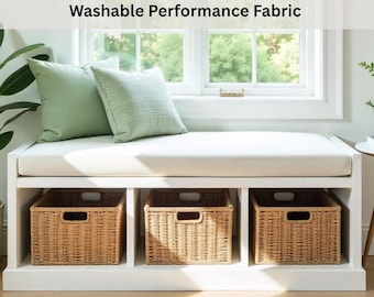 May include: A white wooden bench with a 3-inch thick cushion and three woven wicker storage baskets underneath. Two light green square pillows rest on the cushion. Text reads: 3" Inch Thick Custom Bench Cushion - Washable Performance Fabric.