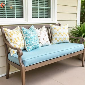 May include: A brown wooden bench with a light blue seat cushion and four decorative throw pillows. The pillows feature patterns in yellow, white, and blue. The text KRAFT CUSHIONS is visible in the upper left corner of the image.