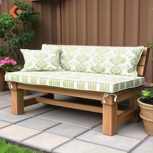 May include: A wooden bench with a green and white striped cushion and two matching pillows. The bench is on a patio with a stone floor. The text "KRAFT CUSHIONS" is visible on the bench.