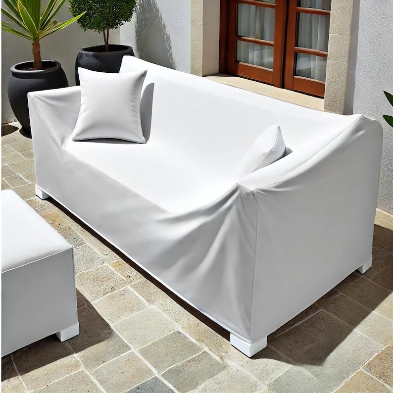 Milk white outdoor furniture cover snugly fitted over a patio dining table and chair set. The cover is sleek, water-resistant, and durable, set against a wooden deck with greenery in the background, emphasizing weather resistance and style
