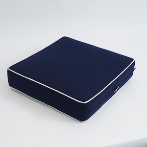 May include: A navy blue square cushion with white piping around the edges. The cushion is made of a soft, durable fabric and is perfect for adding a touch of style to any room.