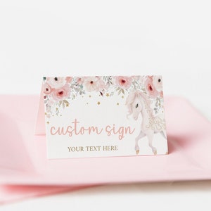 May include: A printable pink and white sign with a floral design and a unicorn illustration. The sign says "custom sign" and "your text here".