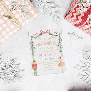 May include: A pink and green Christmas-themed invitation with a Nutcracker and a ballerina. The invitation reads "It's the most wonderful time of the year. Join us to celebrate Makenzie's 1st birthday. Saturday, December 9th at 2pm. Sophia's House, 1234 Main St, Dallas, Texas.  03-456-7590"