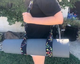 May include: A person carrying a gray yoga mat with a black and rainbow patterned strap.