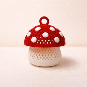 May include: A whimsical mushroom-shaped decorative object. The top is red with white polka dots and a small loop. The base is white with a lattice design. The object is likely a decorative item or a small container.