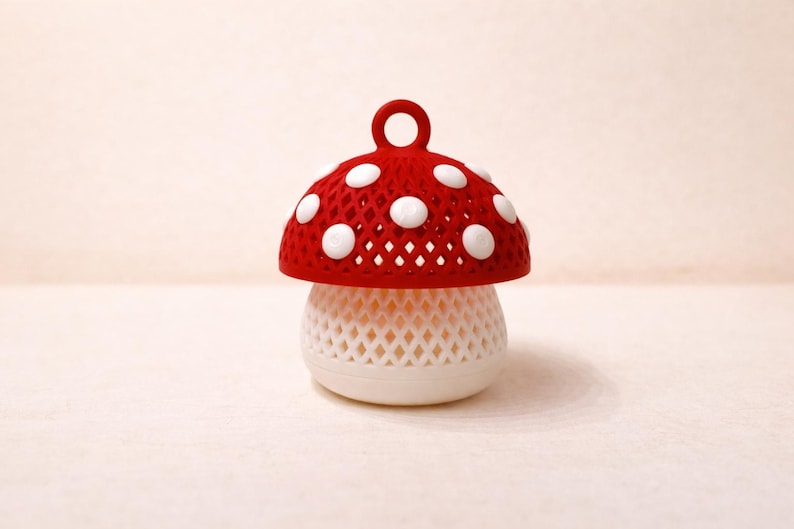 May include: A whimsical mushroom-shaped decorative object. The top is red with white polka dots and a small loop. The base is white with a lattice design. The object is likely a decorative item or a small container.