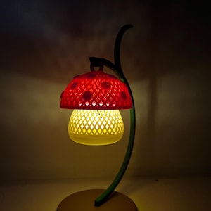 May include: A whimsical mushroom-shaped lamp with a red, perforated cap and a yellow, diamond-patterned shade. The lamp has a green, curved stem and a round, tan base. The lamp is lit, casting a warm glow.