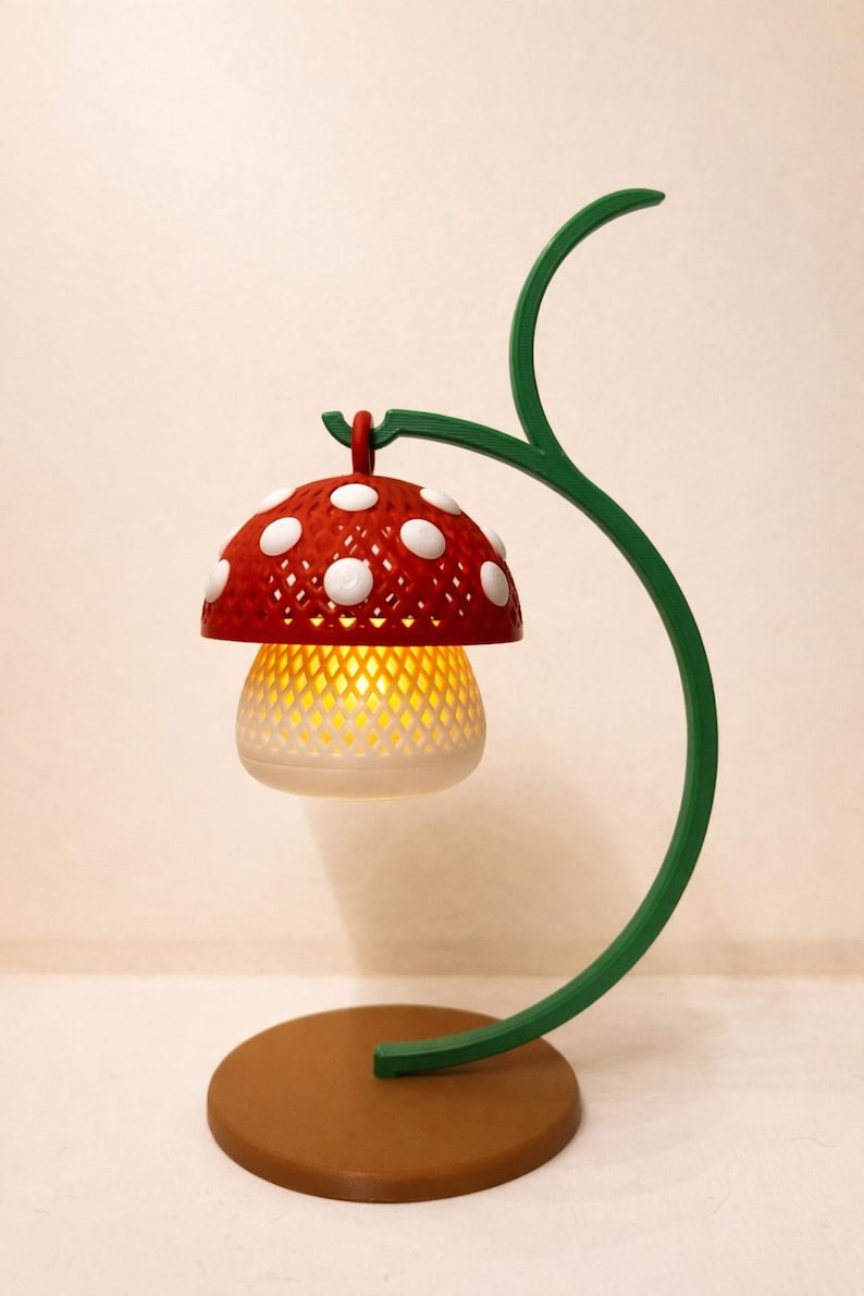 May include: A whimsical mushroom-shaped lamp with a red cap adorned with white polka dots. The lamp features a white, latticed body that emits a warm, yellow glow. It is supported by a green, curved stem and a brown circular base.