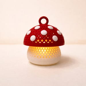 May include: A decorative mushroom-shaped lamp with a red cap featuring white polka dots. The lamp's base is white and has a lattice design, emitting a warm, yellow glow. The lamp has a small loop at the top.