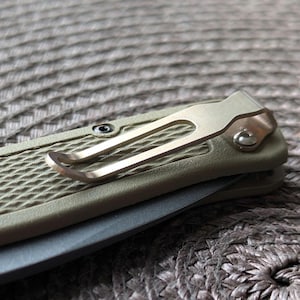 May include: A close-up of a pocket knife with a green handle and a silver pocket clip. The handle has a textured pattern.
