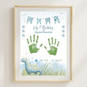 May include: A framed print for a first birthday, featuring green handprints, a blue dinosaur illustration, and text that reads "My 1st Birthday Magical Memories." The print includes the name "Alfie" and age "1 year old."