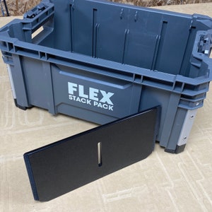 May include: A grey plastic storage container with the text "FLEX STACK PACK" printed on the side. The container is open and a black plastic divider is partially inserted into the container.