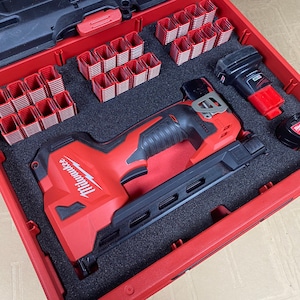 May include: A red Milwaukee brand nail gun in a red and black carrying case with a foam interior. The case also contains a variety of nails and a battery pack.