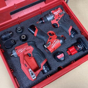 May include: A red tool case with four Milwaukee power tools, including a drill, impact driver, and two batteries. The tools are arranged in a foam-lined case with a red exterior.