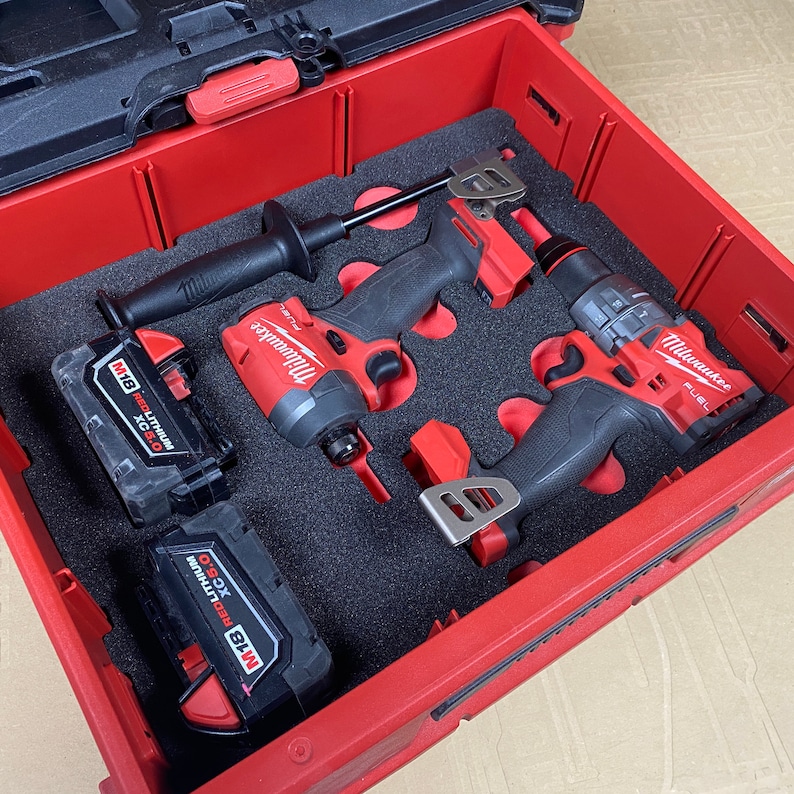 K&ouml;nnte beinhalten: Eine rote und schwarze Werkzeugbox mit zwei Milwaukee-Elektrobohrh&auml;mmern und zwei roten Lithium-Ionen-Akkus. Die Bohrh&auml;mmer sind ein Bohrhammer und ein Schlagschrauber.