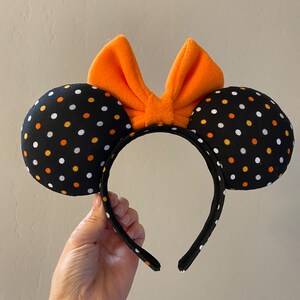 May include: Black and orange polka dot Minnie Mouse ears with an orange bow.