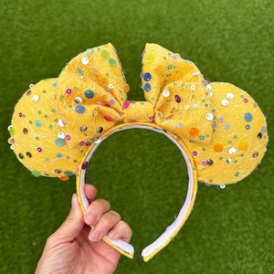 May include: Yellow fabric mouse ears with a bow and colourful sequins.