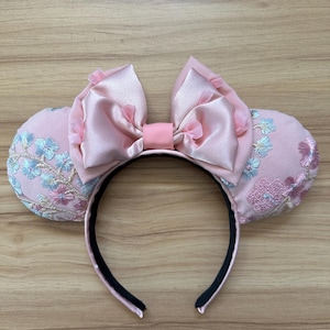 May include: Pink mouse ears headband with a satin bow and floral embroidery.