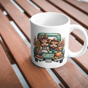 May include: White ceramic mug featuring a teal pickup truck bed with two cartoon cows. The truck bed is filled with pumpkins, sunflowers, and fall foliage. The text "hello fall" is on the truck bed, and "grateful" is on the bumper.