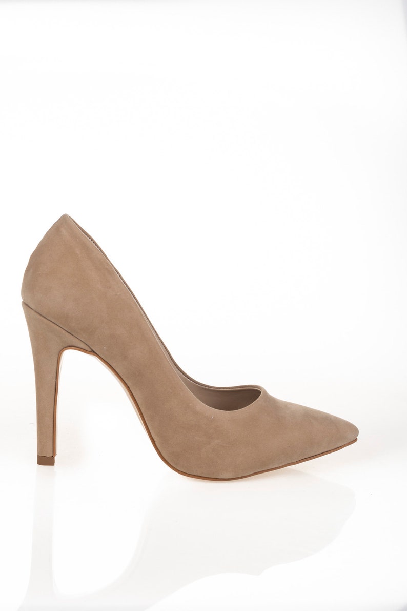 May include: A pair of beige suede high-heeled pumps with a pointed toe.