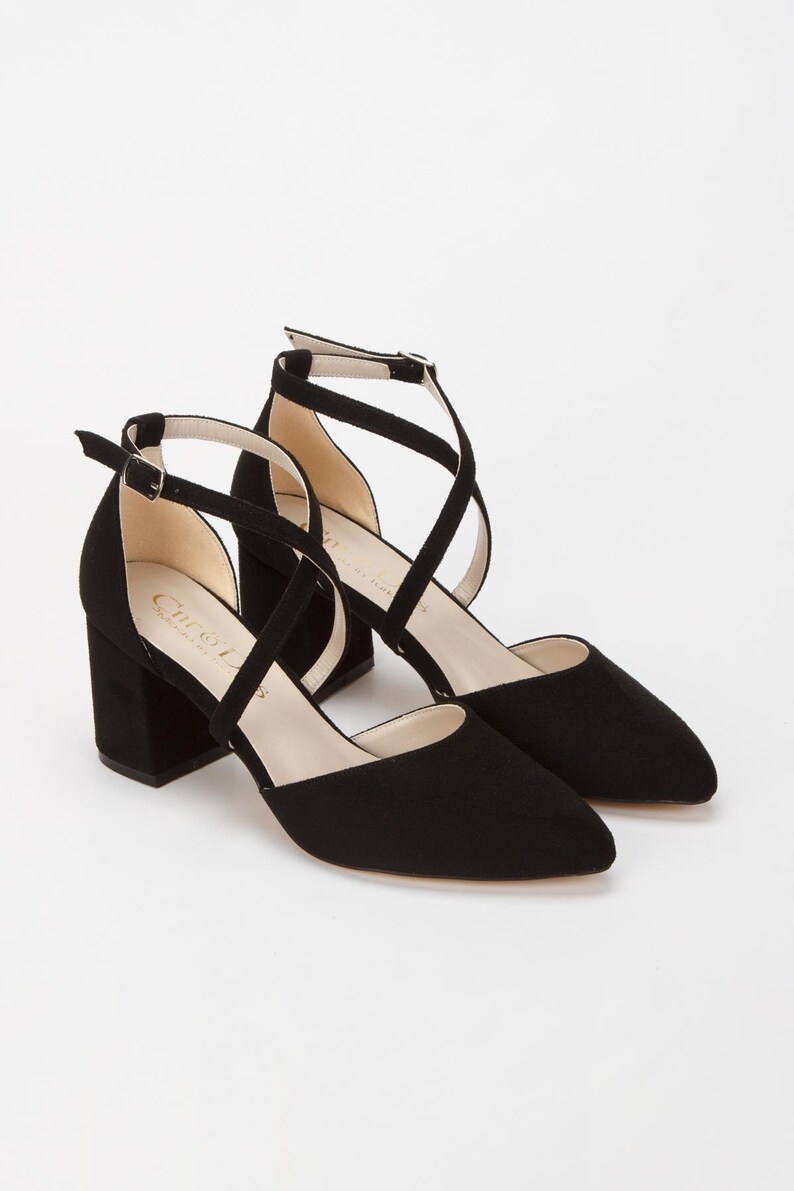 Puede incluir: Zapatos de tac&oacute;n de ante negro con tiras cruzadas y tac&oacute;n de bloque.