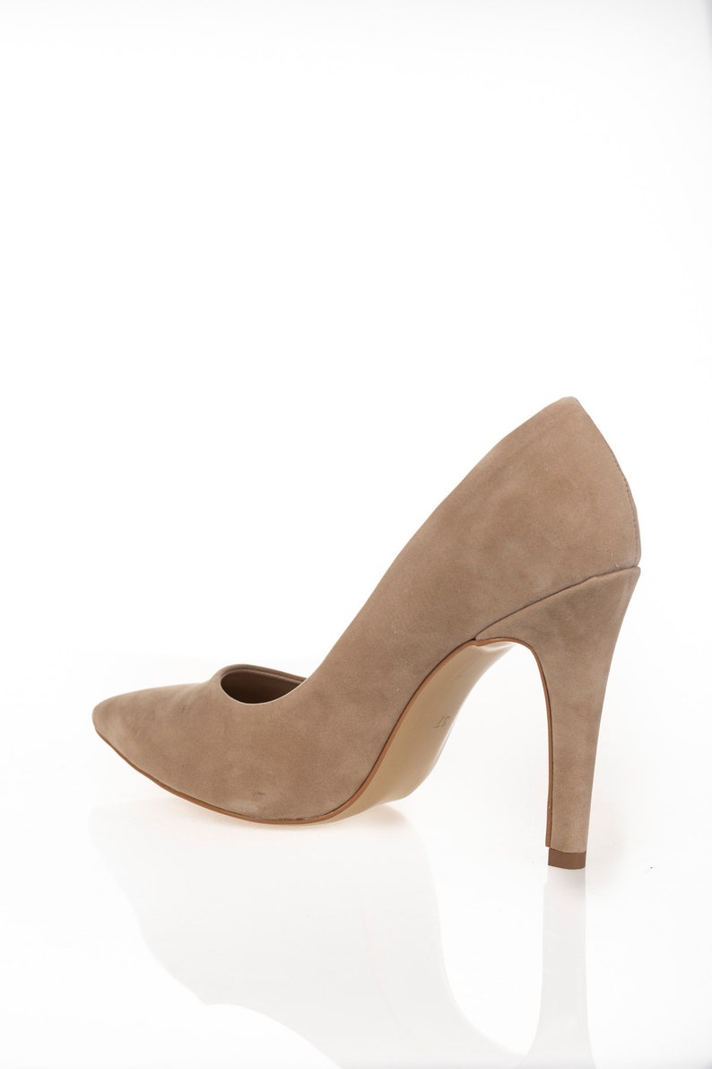 May include: A pair of beige suede high-heeled pumps with a pointed toe.