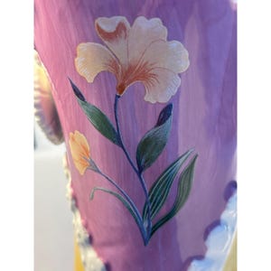 Puede incluir: Un jarr&oacute;n de cer&aacute;mica rosa con un dise&ntilde;o floral. El jarr&oacute;n presenta una flor blanca con un centro rosa y hojas verdes.