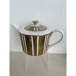 May include: White teapot with gold stripes. The teapot has a lid with a gold knob and a gold rim.