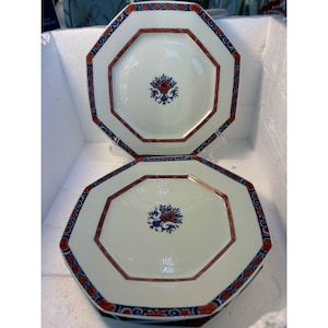 May include: Two octagonal ceramic plates with a white background and a blue and red floral design. The plates have a red and blue border.