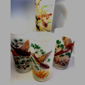 May include: Four frosted drinking glasses with bird illustrations. The glasses feature colorful images of birds in flight, surrounded by green foliage and yellow accents. The glasses have a textured, speckled appearance.