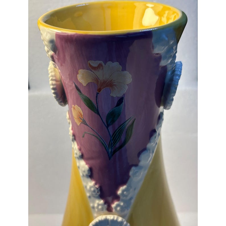 Puede incluir: Un jarr&oacute;n de cer&aacute;mica amarillo y morado con detalles florales blancos y un dise&ntilde;o floral. El jarr&oacute;n tiene una boca ancha y una base estrecha.