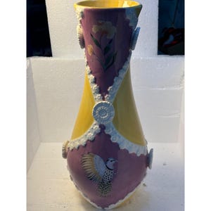 Puede incluir: Un jarr&oacute;n de cer&aacute;mica amarillo y morado con detalles de encaje blanco y un dise&ntilde;o de p&aacute;jaro pintado.