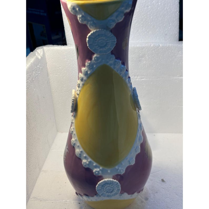 Puede incluir: Un jarr&oacute;n de cer&aacute;mica morado y amarillo con dise&ntilde;os de encaje blanco y acentos circulares blancos.