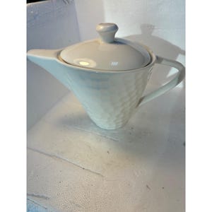 以下が含まれることがあります： 蓋と取っ手がついた白いセラミック製のティーポット。ティーポットは表面がテクスチャ加工されています