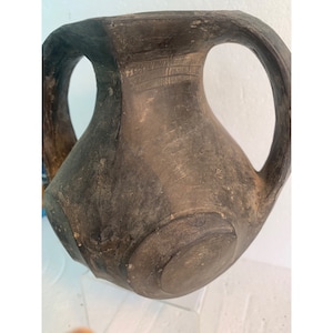 May include: A dark brown, hand-crafted pottery vase with two handles. The vase has a rounded body and a wide, flat base.