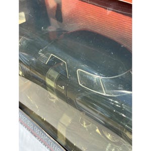 Könnte beinhalten: Ein schwarzes Modellauto in einer transparenten Kunststoff-Vitrine. Das Auto hat ein schlankes Design mit sichtbaren Details wie Fenstern und Türlinien. Die Verpackung trägt den Schriftzug "AKER CUSTOM".