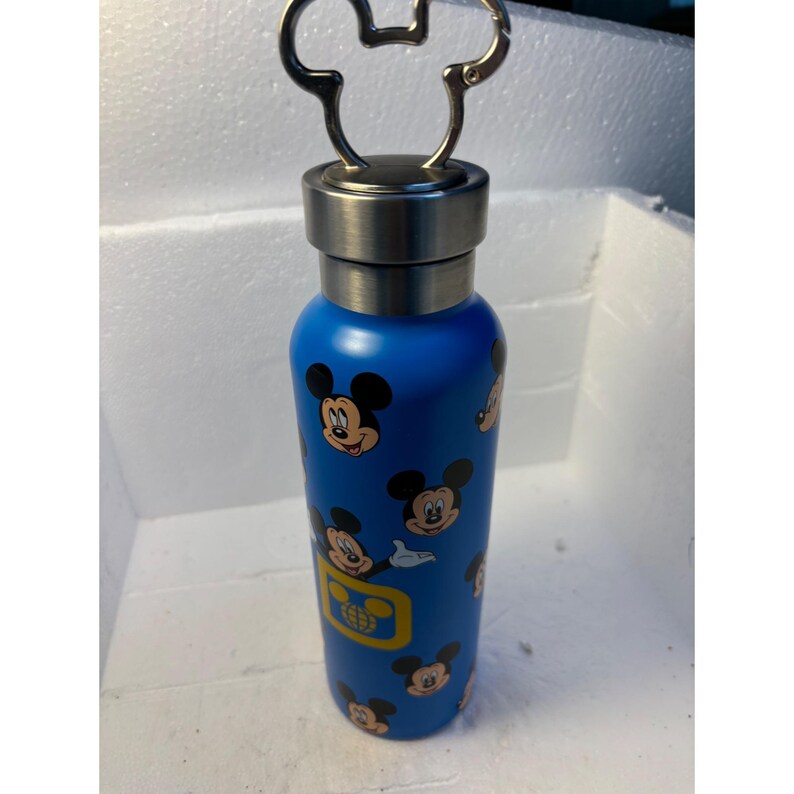 May include: A blue stainless steel water bottle with a Mickey Mouse design. The bottle has a silver lid with a Mickey Mouse shaped handle.