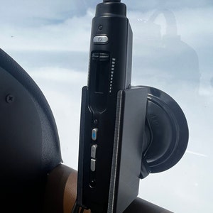 May include: A black car charger with a suction cup mount, a digital display, and multiple buttons. The charger is attached to a car seat.