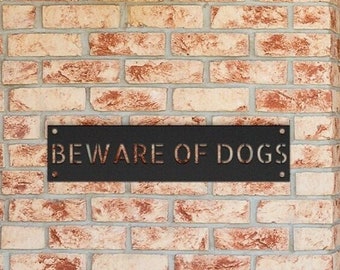 May include: A black metal sign with the text "BEWARE OF DOGS" mounted on a brick wall next to a wooden door with a stained glass window.