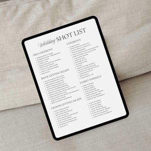 May include: A black tablet shows a wedding shot list, including pre-ceremony, bride getting ready, and ceremony sections. The text is in a classic font. The tablet is placed on a neutral-toned surface.