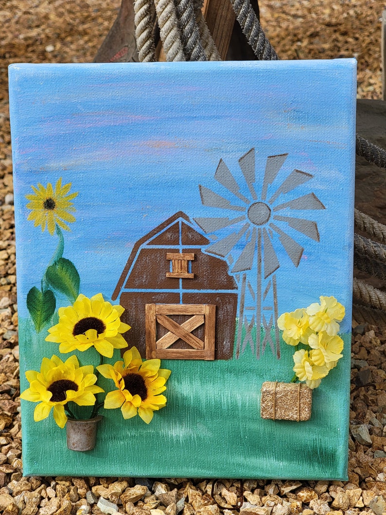 K&ouml;nnte beinhalten: Eine handgemalte Leinwand mit einem braunen Scheunen, einer Windm&uuml;hle und Sonnenblumen. Die Scheune hat eine Holzt&uuml;r und ein Fenster. Die Windm&uuml;hle hat ein graues Fl&uuml;gelrad. Die Sonnenblumen sind gelb mit braunen Zentren. Der Hintergrund ist ein blauer Himmel mit Wolken.