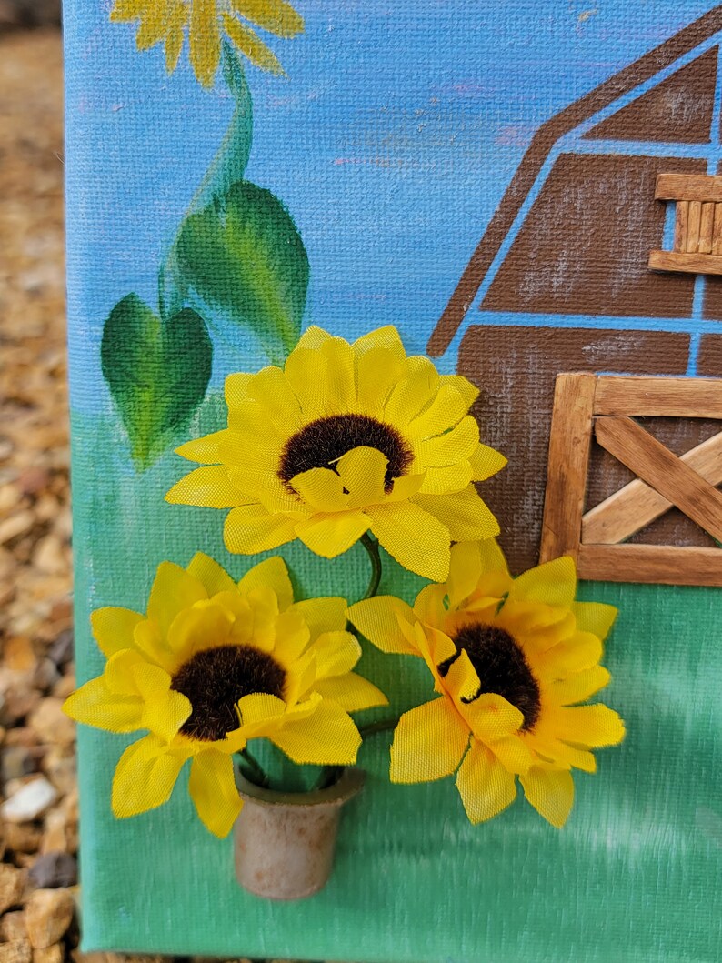 K&ouml;nnte beinhalten: Drei gelbe Sonnenblumen mit braunen Zentren sind in einer Gruppe angeordnet und in einen kleinen braunen Topf gestellt. Die Sonnenblumen sind auf eine Leinwand mit gr&uuml;nem Hintergrund und blauem Himmel im Hintergrund gemalt.