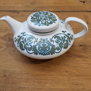 May include: White teapot with a green and blue floral pattern. The teapot has a lid with a matching pattern.