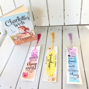 May include: Three watercolor bookmarks with quotes from Charlotte's Web. The first bookmark is pink and orange with the quote "With the right words you can change the world - Charlotte's Web". The second bookmark is yellow and orange with the quote "Let a little sunshine in - Charlotte's Web". The third bookmark is blue and purple with the quote "You have been my friend... that in itself is a tremendous thing - Charlotte's Web".