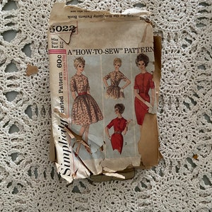 Peut inclure: Un patron de couture vintage Simplicity pour une robe, numéro de modèle 5022, taille 12, tour de poitrine 81 cm. Le patron est intitulé "A "How-To-Sew" Pattern" et comprend des illustrations de trois femmes portant différentes versions de la robe.