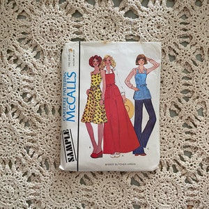 May include: A vintage McCall's sewing pattern envelope with the text "Carefree Patterns" and "McCall's" in a red and white font. The envelope features three women modeling different styles of dresses and an apron. The text "Misses' Butcher Apron" is printed on the bottom of the envelope.