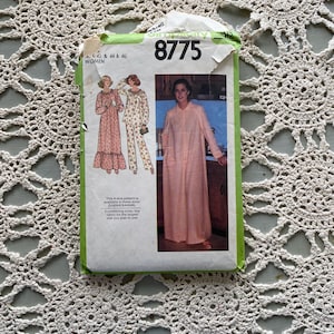 Könnte beinhalten: Ein Vintage-Schnittmusterpaket für Damen, mit einem pfirsichfarbenen Roben-Design. Das Paket ist grün und weiß, mit der Nummer "8775" deutlich sichtbar. Das Muster enthält die Größen 42, 44 und 46. Der Hintergrund ist eine cremefarbene, gehäkelte Spitzendecke.