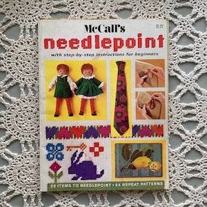 Può includere: Un libro vintage di punto ago McCall's con istruzioni passo passo per principianti. La copertina presenta illustrazioni di bambole, una cravatta floreale e motivi a punto ago. Il titolo "needlepoint" è in lettere rosse.