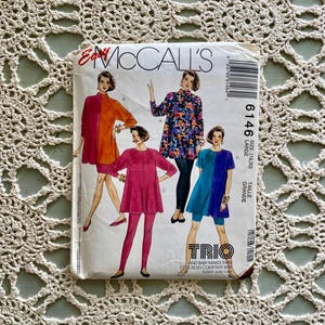 Pode incluir: Um pacote de padrões de costura McCall's vintage com ilustrações de três conjuntos de túnica e leggings. O pacote tem um fundo branco com o texto "Easy McCall's" e o número do padrão 6146. Os conjuntos são em tons de laranja, rosa, azul e floral.