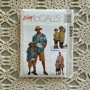 Op de afbeelding: Een vintage McCall's naaipatroon envelop met afbeeldingen van een vader en zoon in bijpassende shirts en shorts. Het patroon is gelabeld "Easy McCall's" en bevat het nummer 2205.
